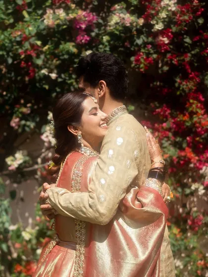 A warm, heartfelt hug between the couple, set against a vibrant wall of bougainvillea. The bride's joyful expression says it all, a perfect candid moment.