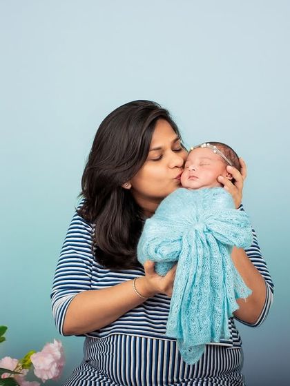 A mother's gentle kiss for her newborn. This simple, clean studio shot with a pop of floral color beautifully captures the tenderness and love of new motherhood.
