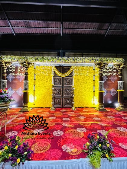 A grand stage for a naming ceremony, featuring a backdrop of yellow flowers and traditional temple-style pillars. The ornate design creates a majestic setting for the event.