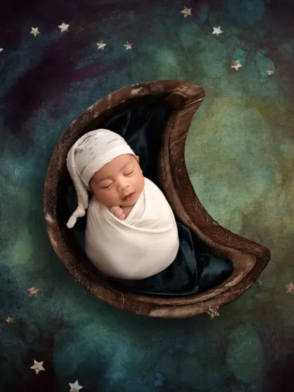 I love you to the moon and back. This composite image places a safely swaddled newborn into a crescent moon prop against a starry night sky.