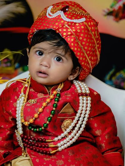 A close-up of a toddler dressed in a traditional red sherwani.