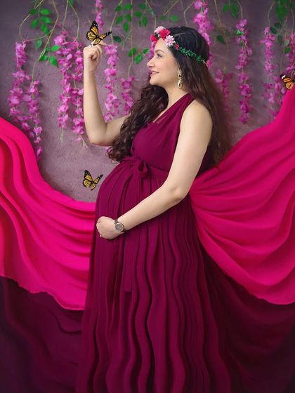 Feeling like a goddess in this whimsical studio setup. The flowing magenta gown, flower crown, and magical butterflies create a truly enchanting maternity portrait.
