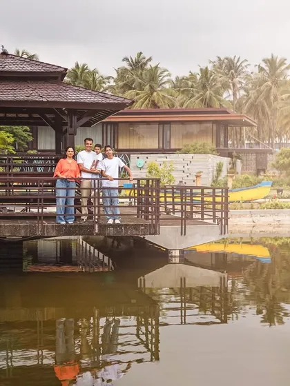 A family stands together on a wooden gazebo overlooking a pond, creating a beautiful reflection. This wide shot captures the serene atmosphere of their outdoor family portrait session.