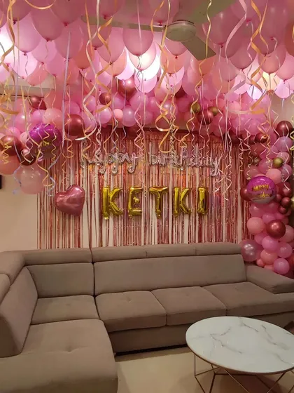 This birthday setup fills the room with shades of pink and rose gold balloons. The decoration covers the ceiling and frames the main wall, which features a shimmer curtain and 'Happy Birthday' foil letters.