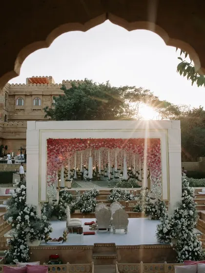 The sun sets behind a magnificent floral mandap, framed perfectly by a palace archway. This shot highlights our focus on creating picture-perfect moments where light and decor work in harmony.