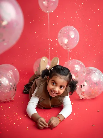 A fun and energetic shot with a bright red background and glittery balloons. Perfect for a toddler with lots of personality!