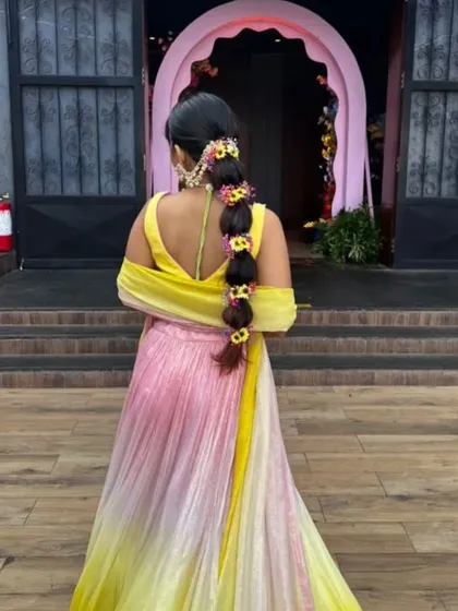A back view of a bride with a bubble braid adorned with colorful flowers for her Mehendi ceremony. This hairstyle is fun, vibrant, and perfect for a daytime event.