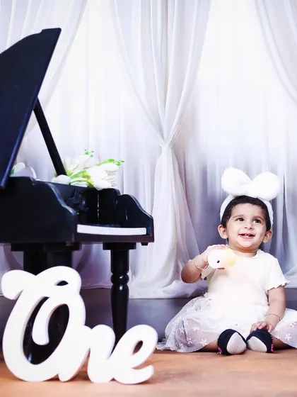 A sweet, smiling baby girl enjoying her first birthday piano-themed photoshoot.