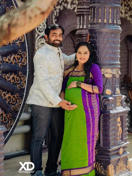 A smiling couple posing against an intricately carved pillar, blending their modern style with traditional architectural elements.