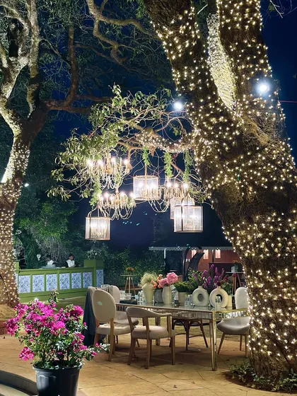 Fairy lights and chandeliers transform the trees into a magical dining canopy for an outdoor wedding reception. The design blends the natural environment with luxurious lighting for an enchanting evening.