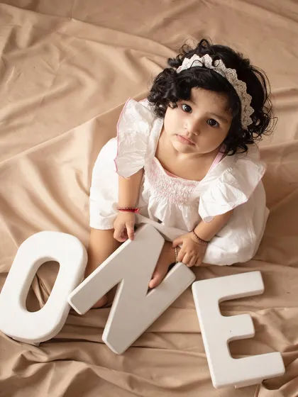 Celebrating turning one. This little girl sits with large letters spelling "ONE" for a classic first birthday photo.