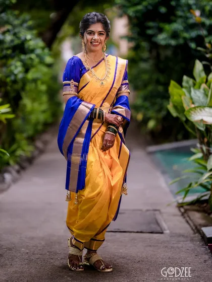 A full view of the bride in her yellow and blue Nauvari saree, a classic and vibrant choice for a Maharashtrian wedding.