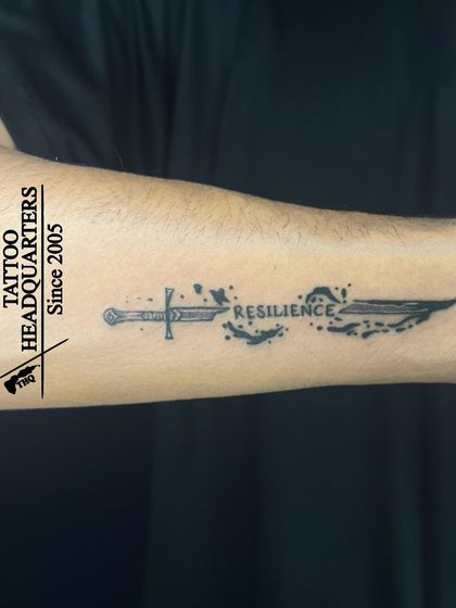 A creative tattoo of a sword transforming into the word "RESILIENCE," symbolizing strength and overcoming adversity.