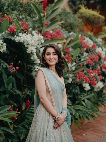 The bride's radiant smile is the centerpiece of this portrait, set against a vibrant backdrop of red and white flowers.