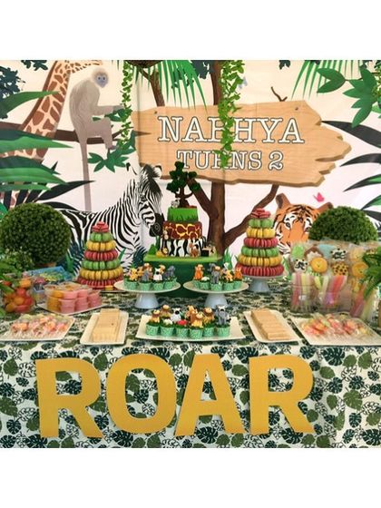 A "ROAR" safari dessert table for a twins' birthday. The setup included a jungle-themed backdrop, animal-topped cakes, and macaron towers, bringing the wild to the party.