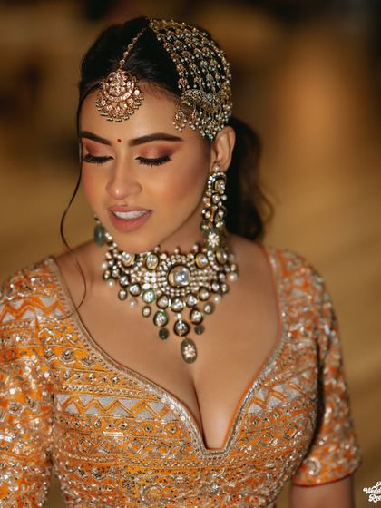 A beautiful close-up of the bride, her makeup and jewelry perfectly complementing her orange and silver lehenga.