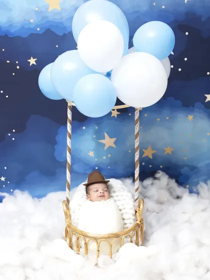 A whimsical hot air balloon adventure is a popular choice for a creative newborn session. This wide shot shows the complete setup, with the baby safely nestled in a basket floating among fluffy clouds and a starry night sky.