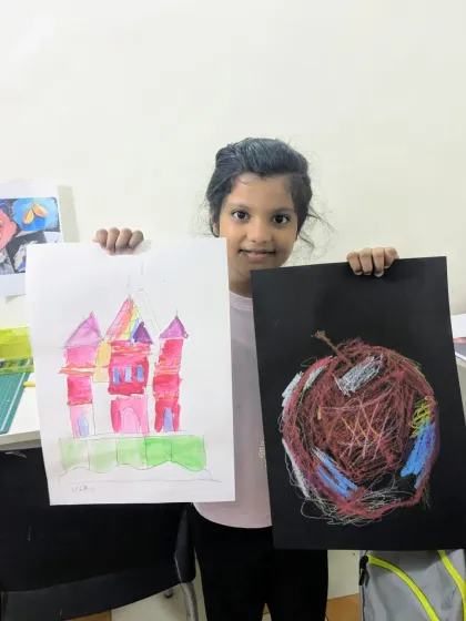 Exploring different styles and mediums. Here, a student shows her vibrant castle painting alongside a creative scribble art apple, learning about color and texture.