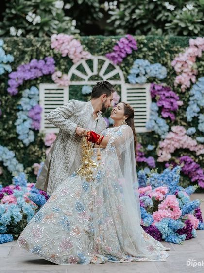 A couple dancing against a beautiful floral backdrop during their Haldi ceremony in Jaipur. The bride's traditional kaleeras add a significant cultural detail to the photo.
