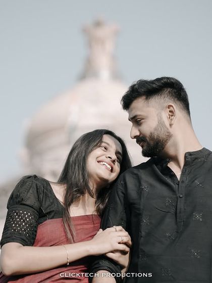 A romantic shot of a couple in traditional black and red outfits, with the Ashoka emblem of Vidhana Soudha in the background.
