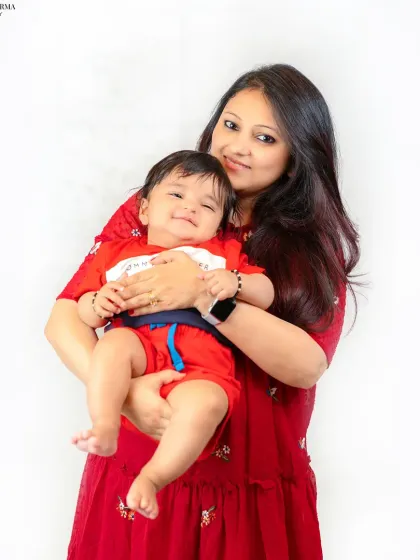 A mother holds her smiling baby, both dressed in cheerful red. This portrait radiates warmth and the sweet, cuddly nature of their bond.