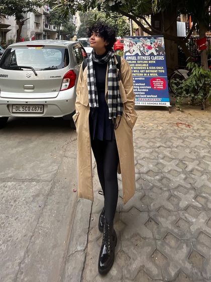 A daytime look with the same trench coat, this time styled with a plaid scarf for a classic, preppy touch.