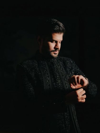 A classic, moody portrait of the groom, looking down as he adjusts his cuff, captured in a low-key lighting style.