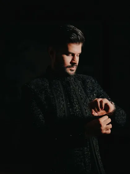 A classic, moody portrait of the groom, looking down as he adjusts his cuff, captured in a low-key lighting style.