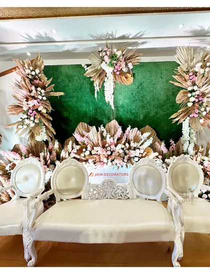 A full view of the rustic-chic stage, showing the beautiful contrast between the green backdrop, the earthy tones of the dried florals, and the elegant white seating.