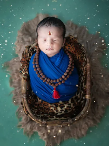 A serene and divine portrait for Mahashivratri. This newborn is styled as a tiny devotee of Lord Shiva, complete with a rudraksha necklace and a blue wrap.