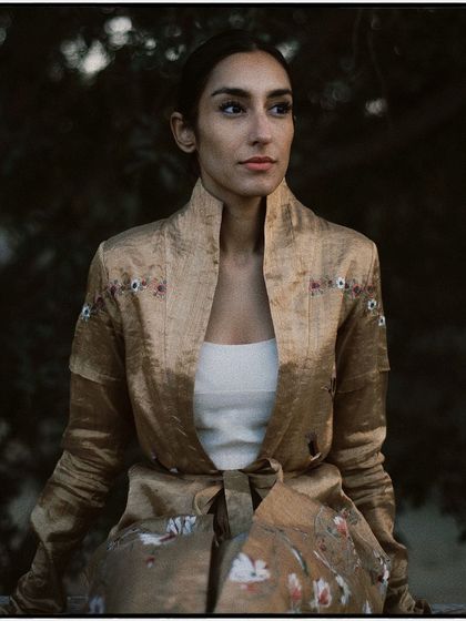 A portrait showcasing an elegant, embroidered jacket. The soft, evening light and the model's poised expression create a timeless and sophisticated image.