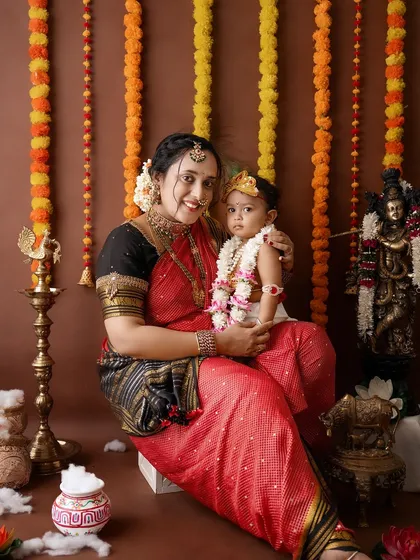 A full, seated portrait showing the beautiful coordination between the mother's saree and the baby's Krishna costume.