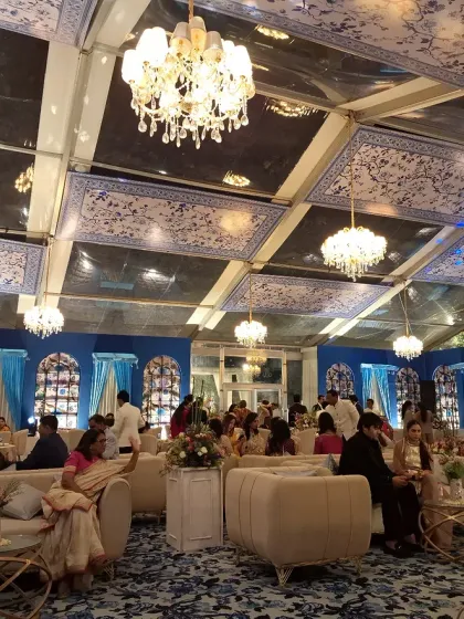 A wide view of a blue and white themed reception, with a custom printed ceiling, elegant chandeliers, and comfortable lounge seating for guests.