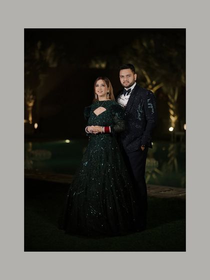 A classic full-length portrait of the couple at their reception. The dark, outdoor setting with subtle lighting creates a sophisticated and romantic atmosphere.