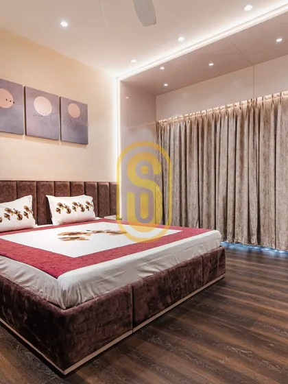 A bedroom featuring a rich, dark wood floor and a plush, channel-tufted velvet headboard. The indirect lighting from the false ceiling and beneath the curtains creates a warm and relaxing mood.