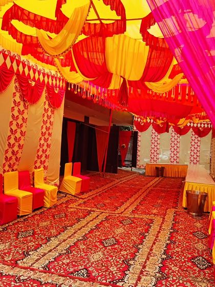 An elegant tent setup for a housewarming, with red and yellow drapes, patterned walls, and organized seating.