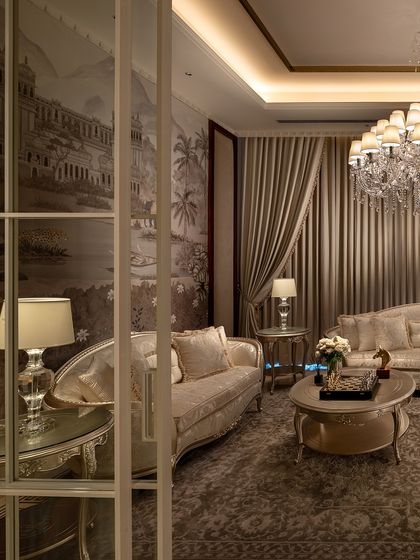 Every detail in this living room, from the vintage wallpaper depicting a classical landscape to the crystal chandelier, speaks of timeless elegance. This space, part of The Ivory Royale, is designed for those who appreciate the finer things in life.