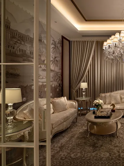 Every detail in this living room, from the vintage wallpaper depicting a classical landscape to the crystal chandelier, speaks of timeless elegance. This space, part of The Ivory Royale, is designed for those who appreciate the finer things in life.