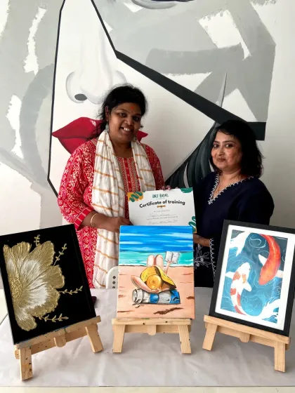 A student receives her certificate of training after completing a short-term course, proudly displaying the three beautiful artworks she created.