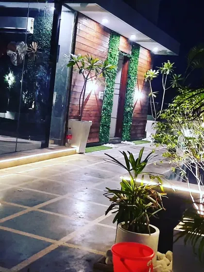 The same glass room at night. The exterior is lit with wall lights and strip lighting, highlighting the wood cladding and vertical gardens.