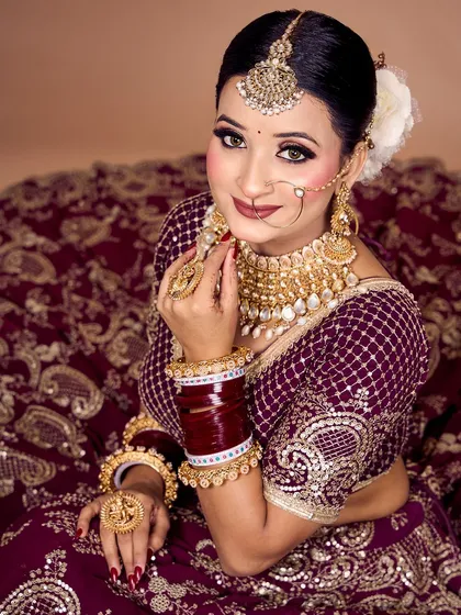 A close-up portrait of a bride in a deep wine-colored lehenga, showcasing the intricate embroidery on the blouse and the matching jewelry.