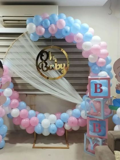A sweet gender reveal or baby shower setup using a circular frame with white draping. The pink and blue balloons, 'Oh Baby' sign, character cutouts, and 'BABY' blocks create a playful and charming look.
