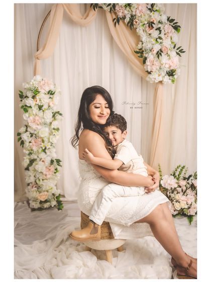 A mother embraces her son in a warm hug during a studio session with a beautiful floral arch. This photo radiates love and comfort, a perfect capture of the mother-child bond.