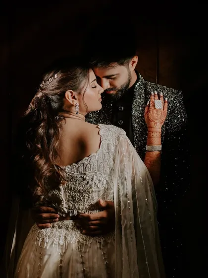 A close, intimate embrace captured in low light. The lighting beautifully highlights the intricate details of the bride-to-be's outfit and the couple's connection.