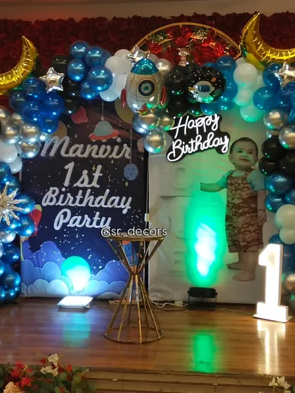 We bring themes to life with custom setups like this space adventure for a first birthday, featuring a personalized backdrop, rocket and planet foil balloons, and a light-up number '1' to mark the special milestone.