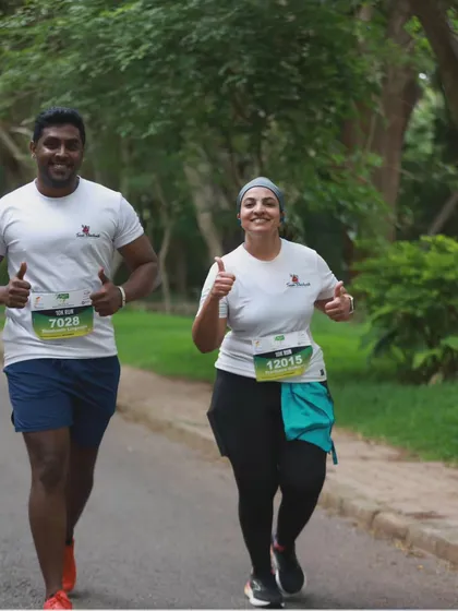 Two team members running side by side, giving a thumbs up during the Mysuru Run. The support of a teammate makes the journey easier.