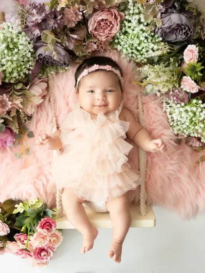 A happy baby girl smiles from her swing, which is adorned with a lush arrangement of pink, purple, and white flowers. This is one of our most popular and joyful setups.