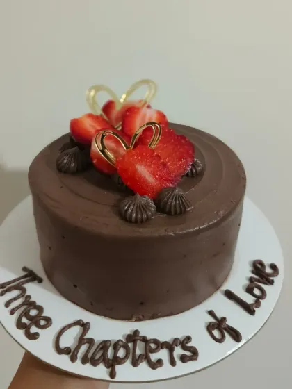 A rich chocolate anniversary cake for "Three Chapters of Love," topped with fresh strawberries.