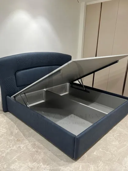 This bed in a deep navy blue features a curved headboard with quilted side panels. It also includes a hydraulic lift mechanism, providing a smart and spacious storage solution.