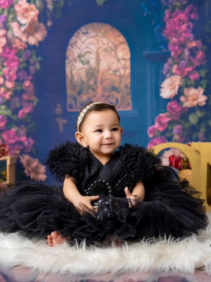 A little fashionista celebrating her first birthday. Sitting on a soft rug in a magical floral setting, this little girl in her black dress is simply precious.